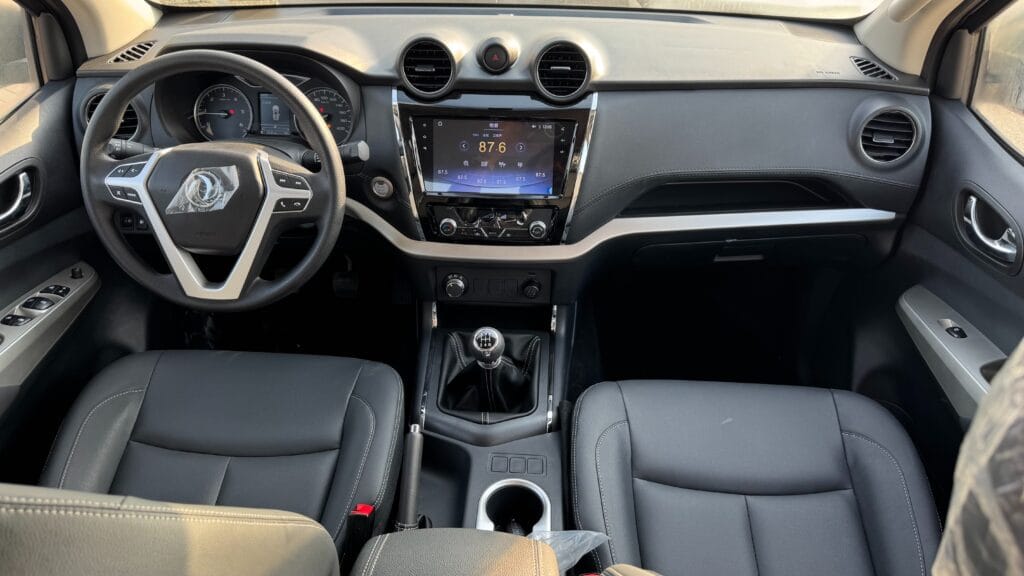 Modern car interior: steering wheel, center touchscreen, and gear shift visible between black leather seats.